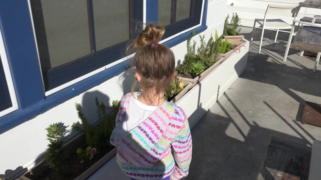 Young girl facing a white planter on a sunny patio.