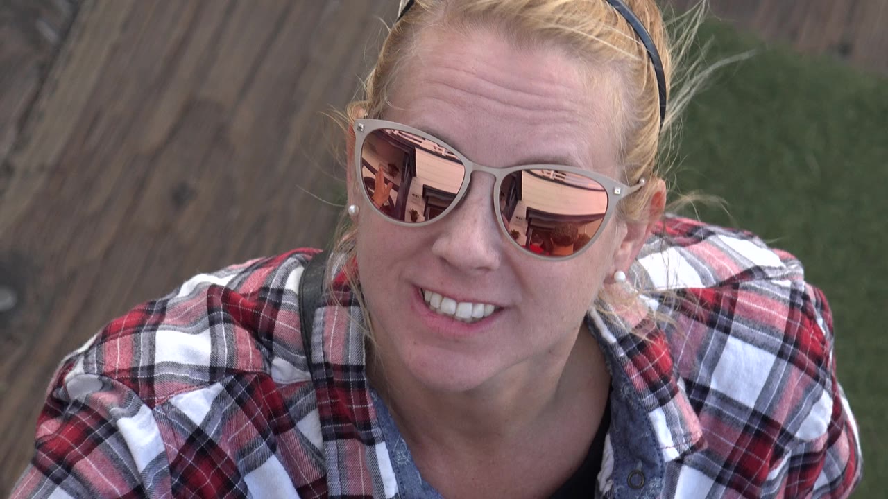 Blonde woman lowers her hand and starts to smile at the camera.