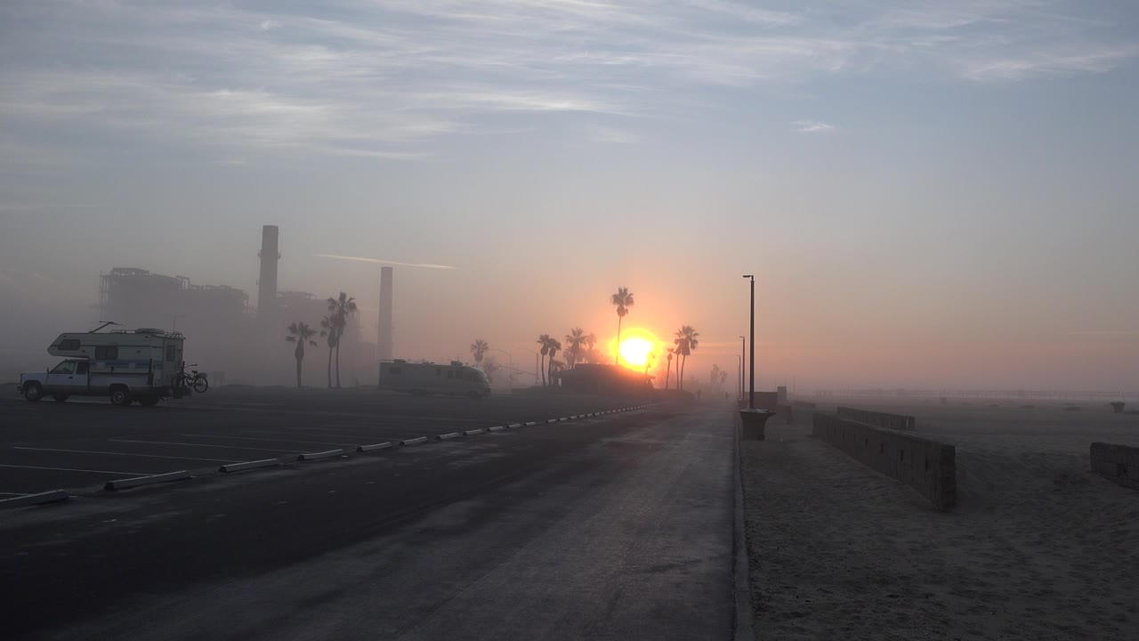 Sunset over a quiet road with palms, haze, and a parked RV.