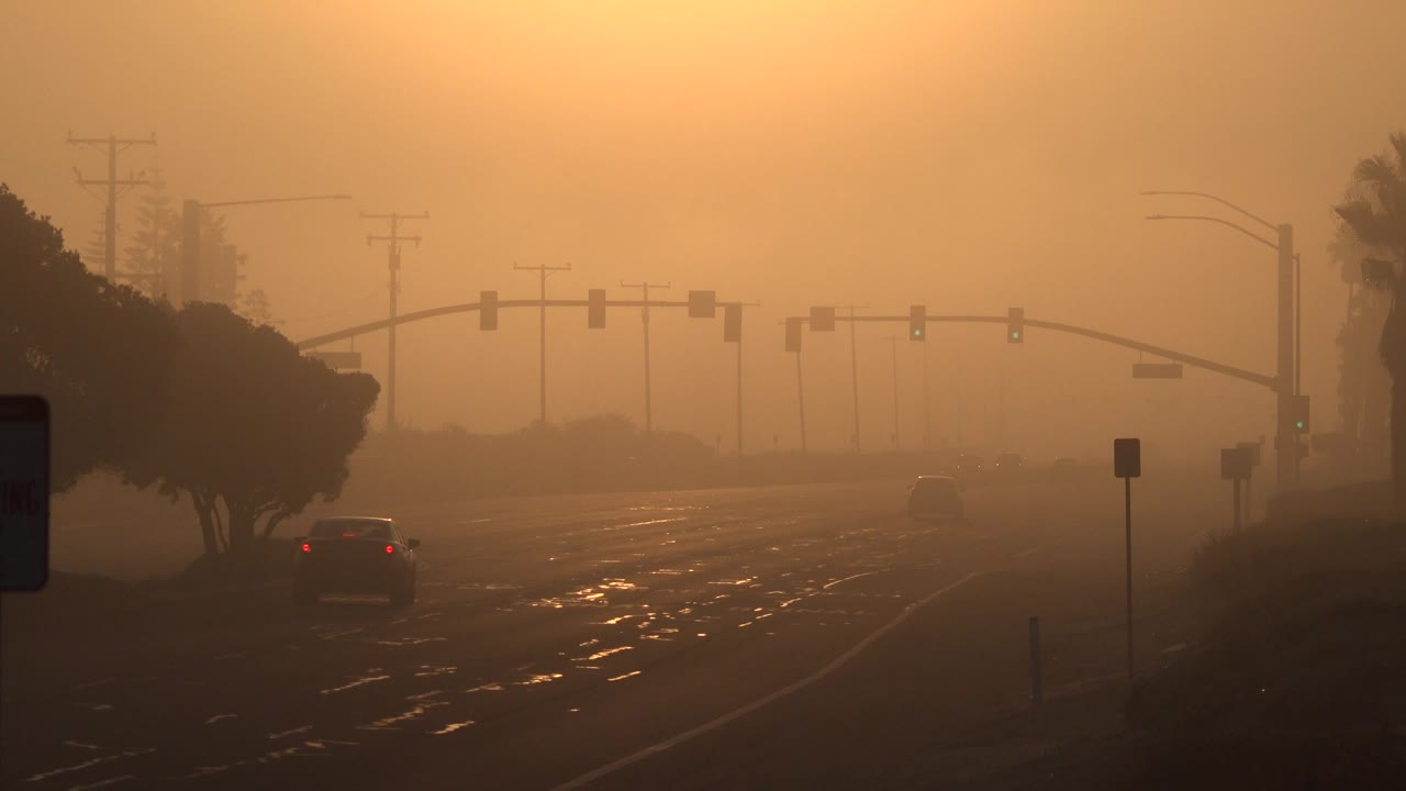 Vehicle drives away on a reflective road under orange haze.