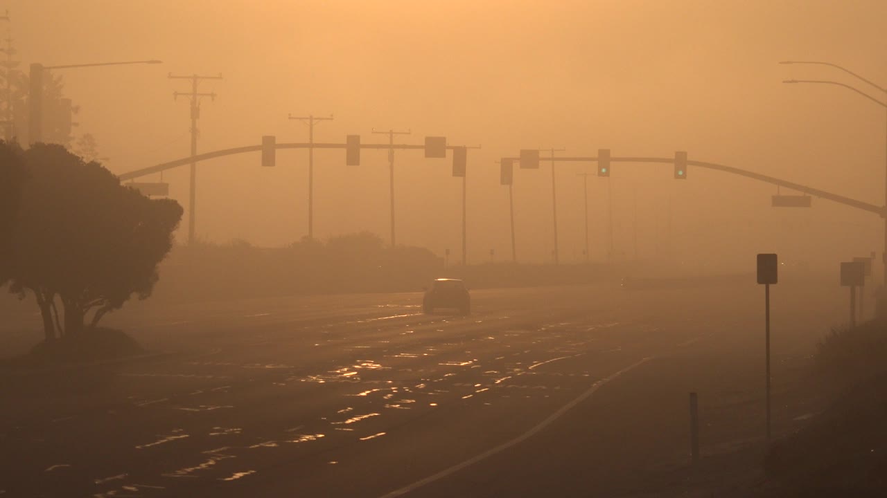 Orange hazy street with traffic lights and a distant car.
