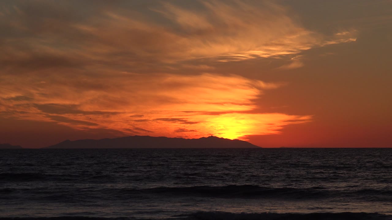 Red-orange sky above ocean waves at sunset.
