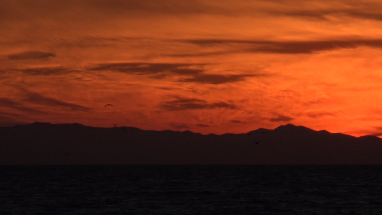 Orange dusk sky over dark ocean and mountain silhouette