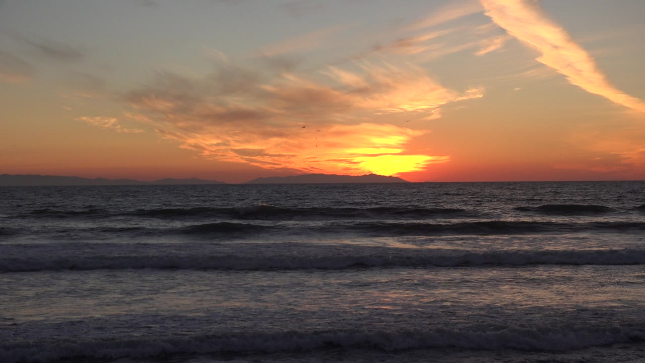 Sunset over ocean waves at Huntington Beach, California, with orange clouds above a dark horizon and no visible people.