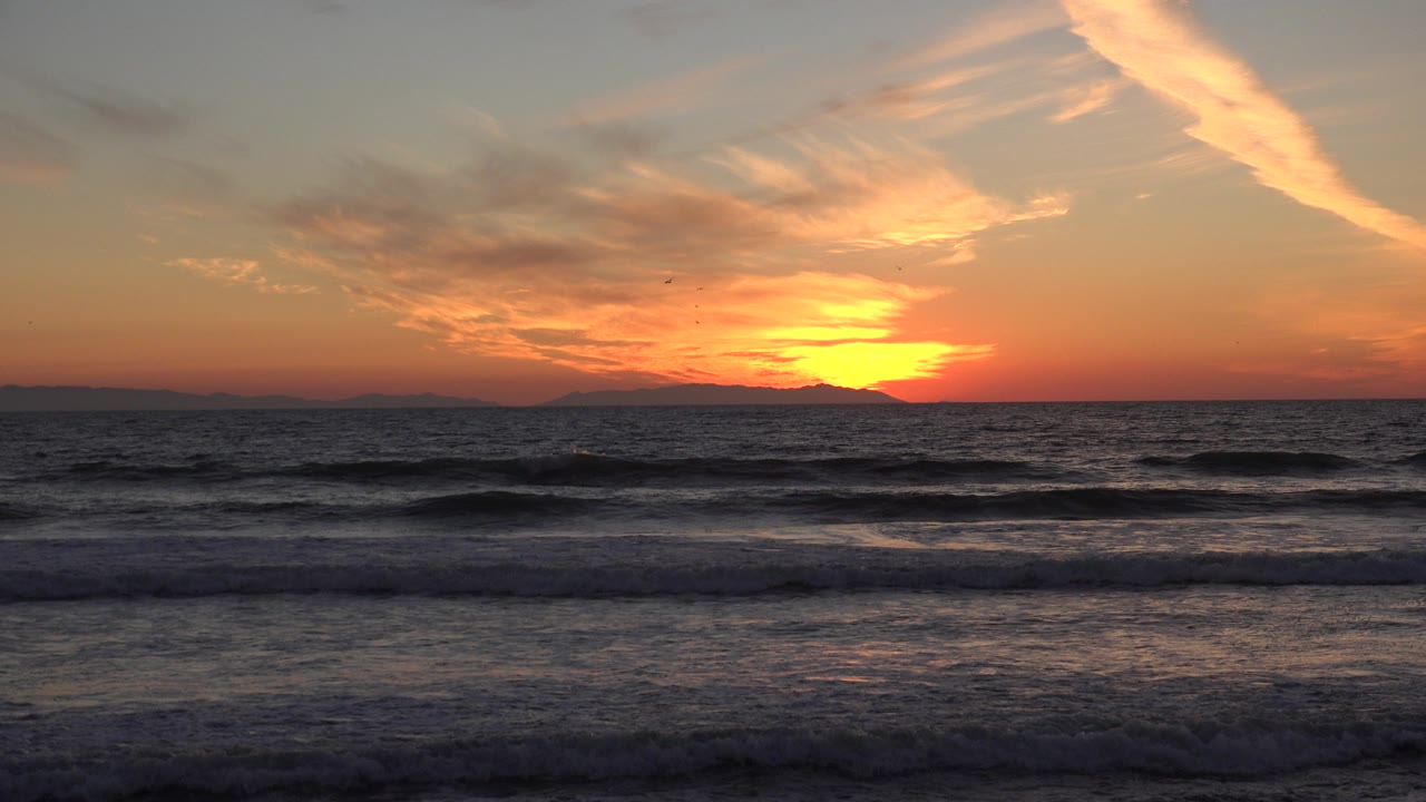 Low orange sun over the Huntington Beach ocean horizon, with layered breaking waves in the foreground and no visible people.