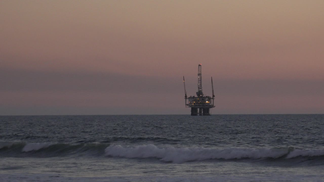 Breaking wave below distant offshore structure at dusk