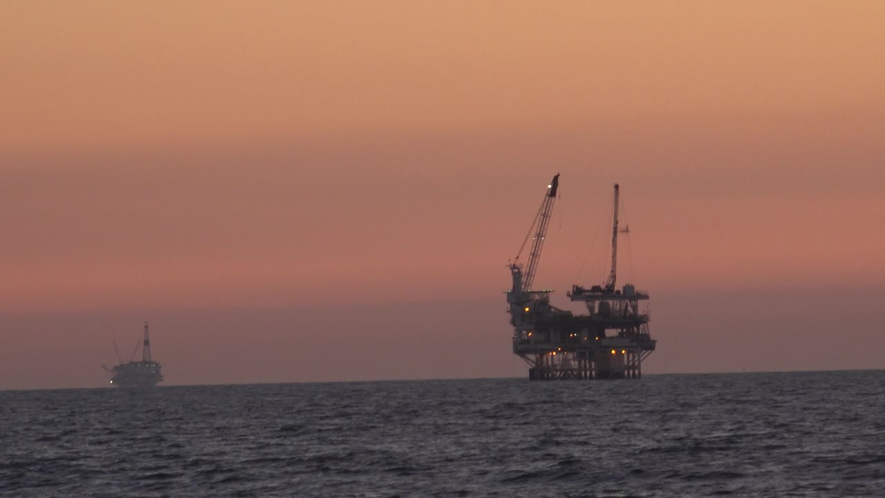 Oil platform with cranes above the horizon and a small vessel to the left.