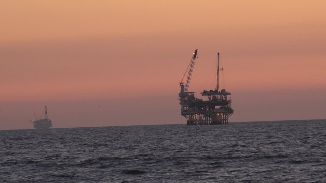 Oil platform lights against a warm sunset horizon.