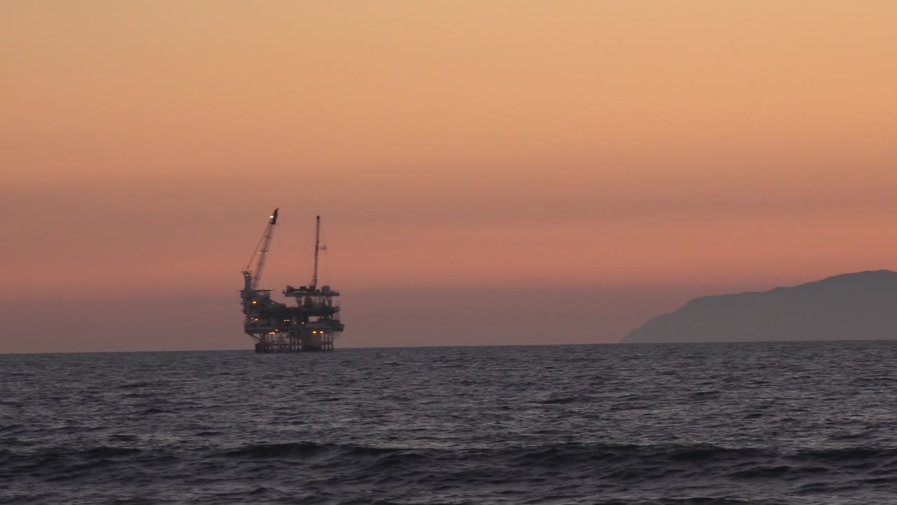 Oil platform remains left of center off Huntington Beach, California, with textured ocean in front, muted orange sky above, and no visible people.