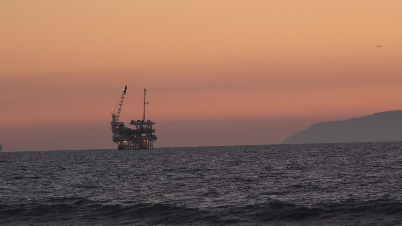 Offshore rig and distant land across dark water at sunset.