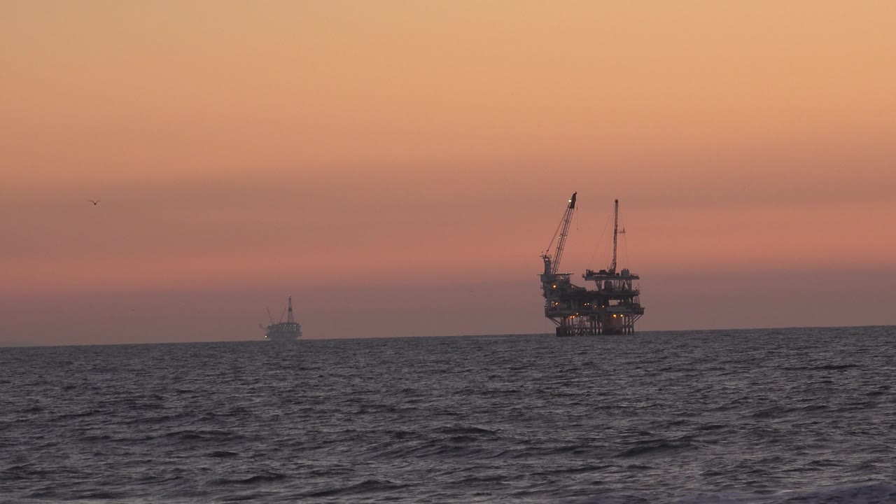 Open sea at sunset with offshore platform silhouette near the right side.