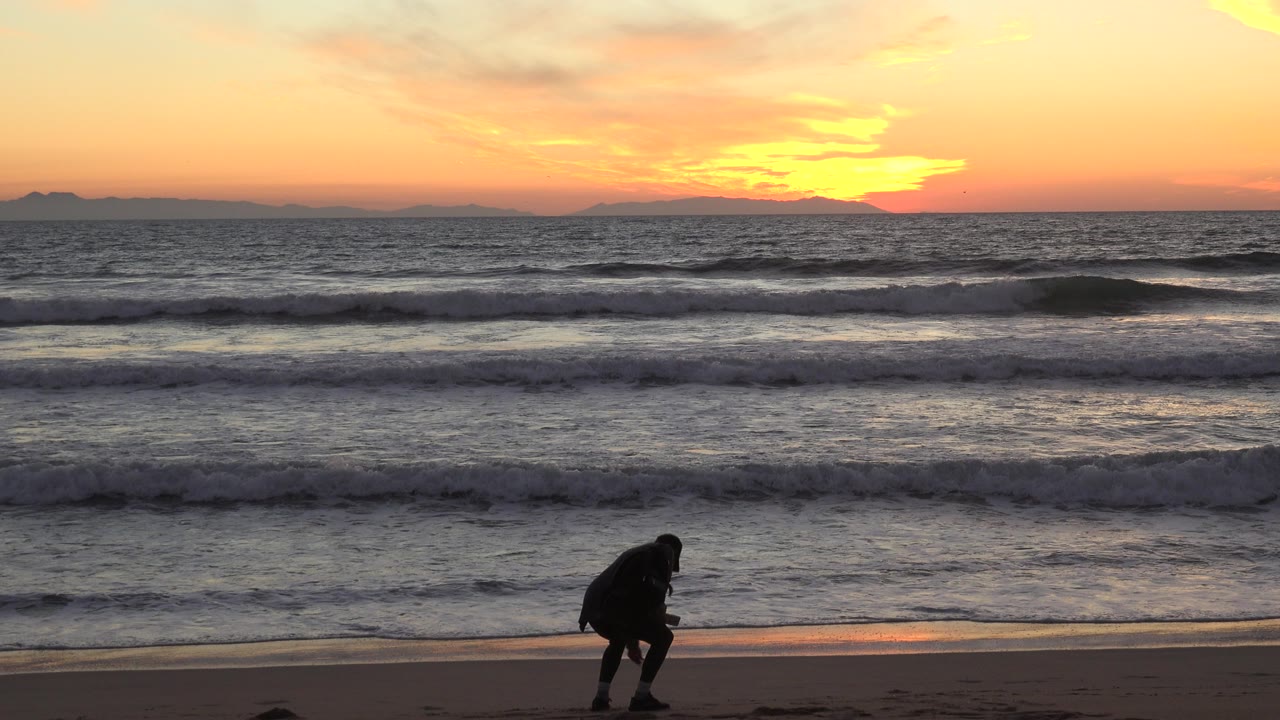 Silhouetted person near the wet sand with sunset waves behind them.