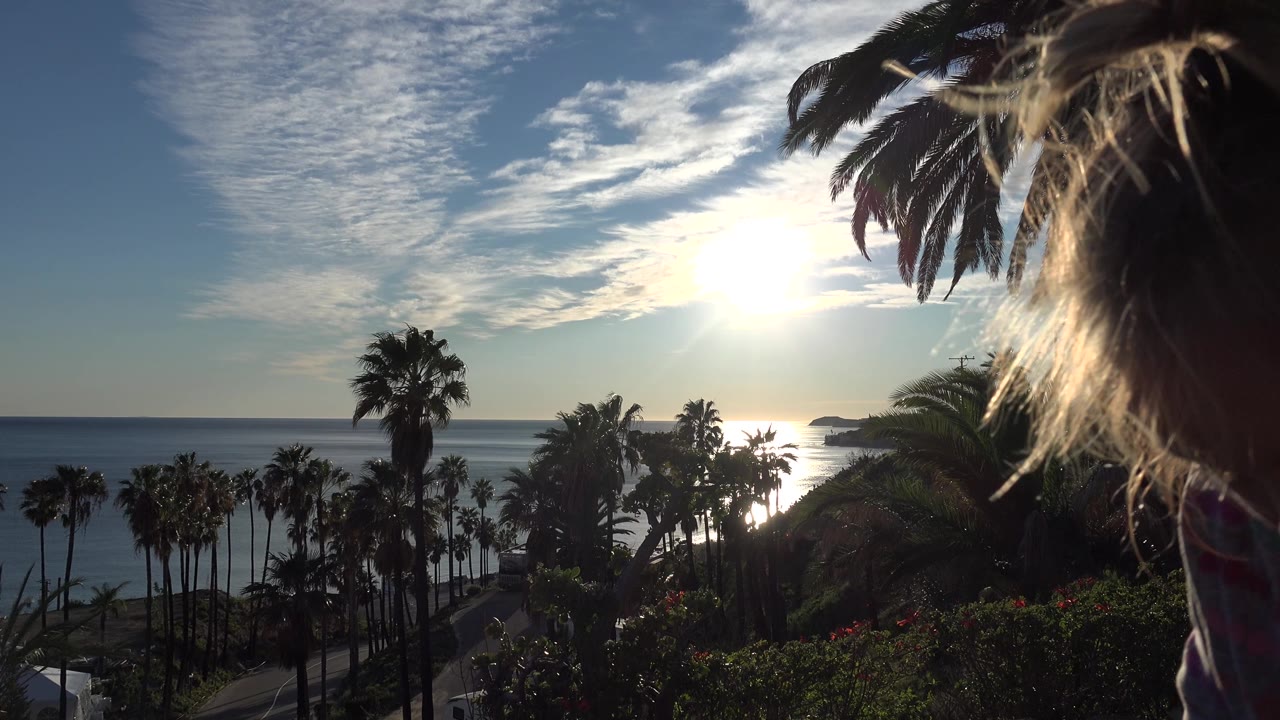 The Huntington Beach ocean view remains backlit by the sun while a partial blond-haired person and shoulder appear at the right edge of the frame.