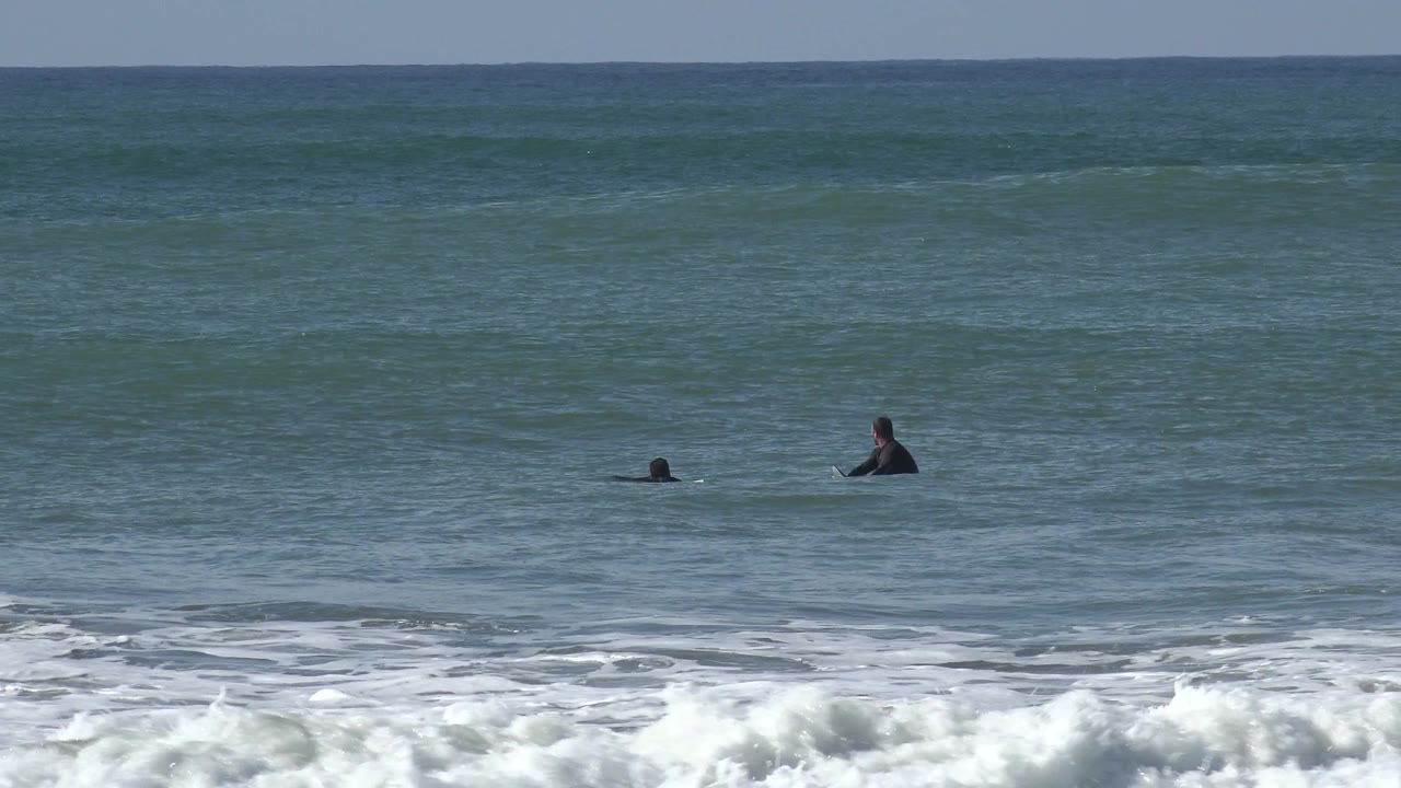 Wide Huntington Beach ocean view with two small surfers waiting offshore and whitewater breaking across the lower frame.