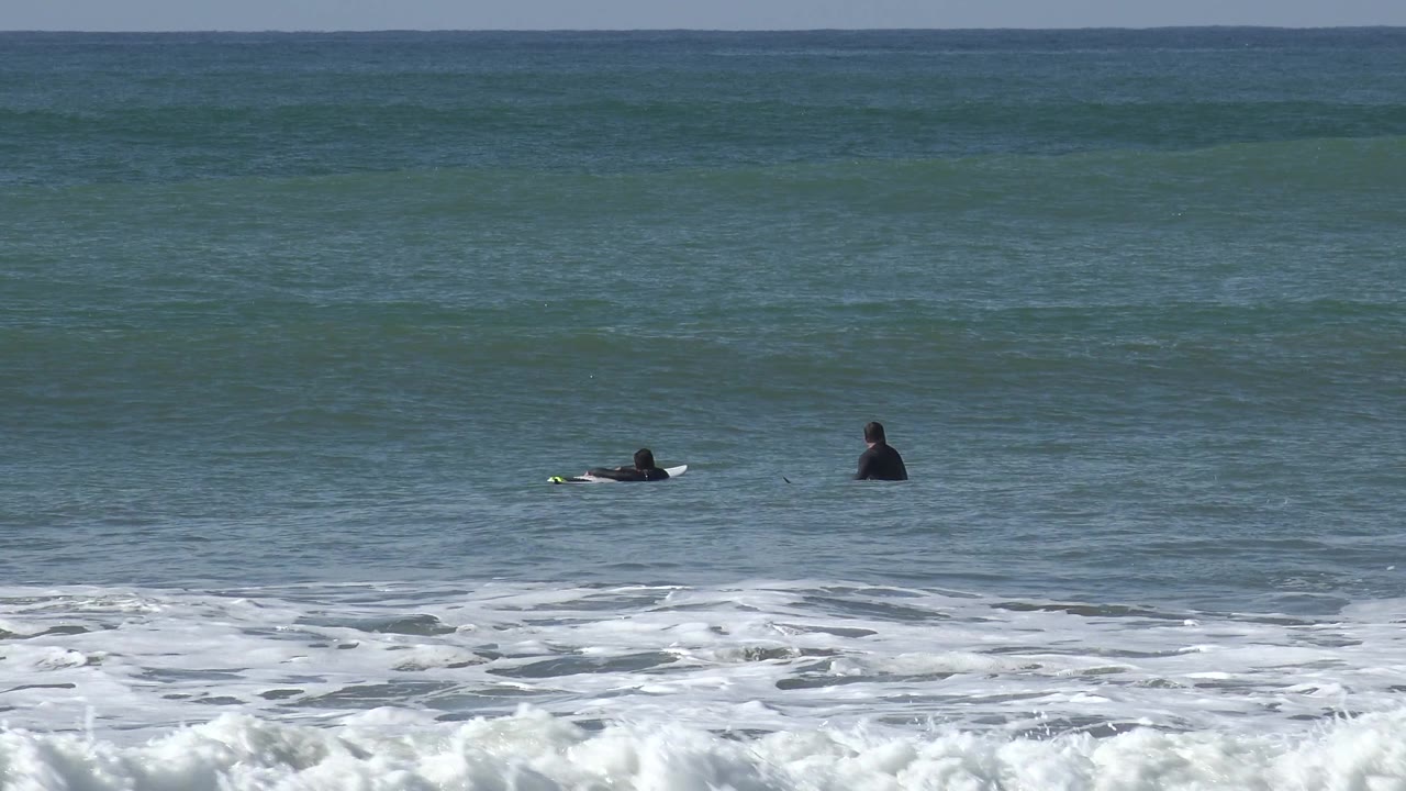 Four distant surfers are visible across the midground ocean.