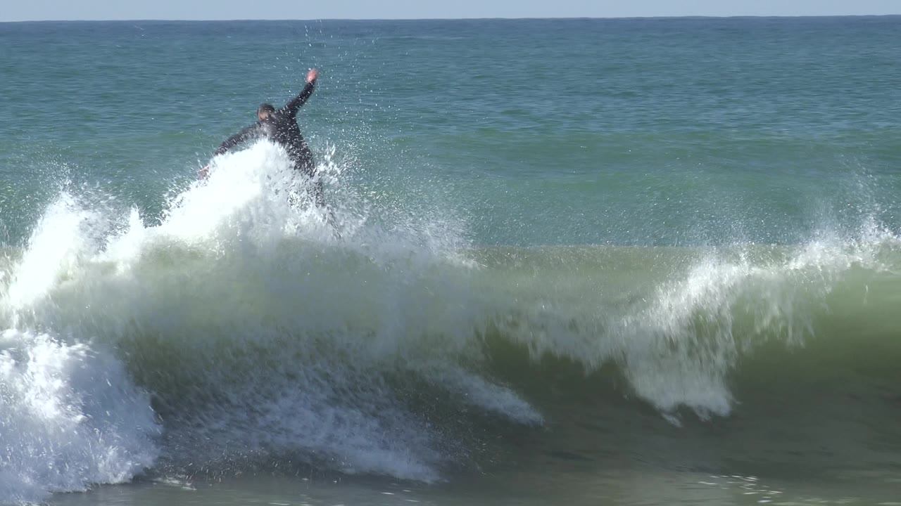 Surfer falls partly behind a burst of whitewater.