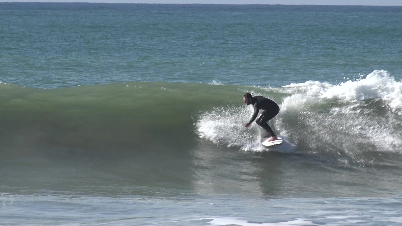 At Huntington Beach, California, the surfer crouches low on a white board as the wave steepens and whitewater curls close behind him.