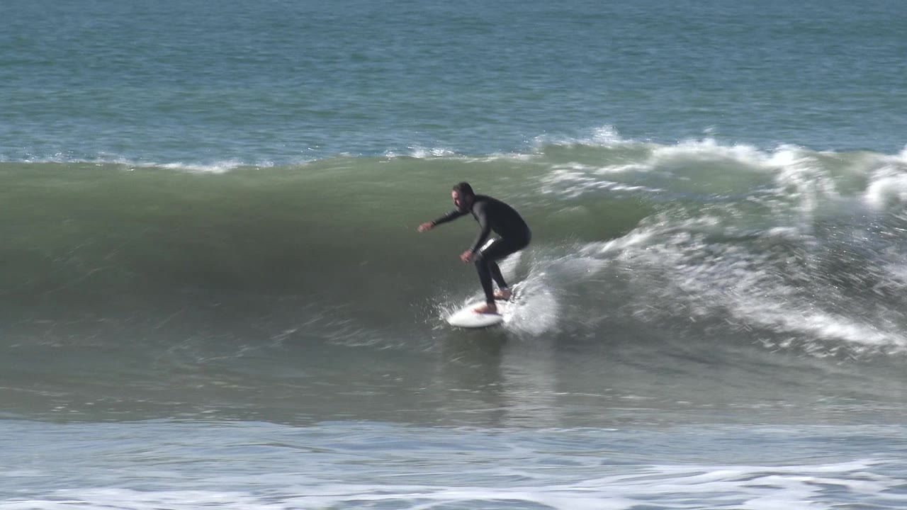 At Huntington Beach, California, the surfer stands more upright on the board near the right side of the breaking wave, with foamy spray rolling behind.