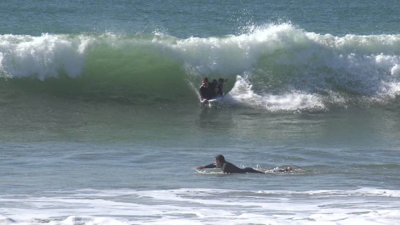 Surfer near a curling wave with a swimmer paddling below.