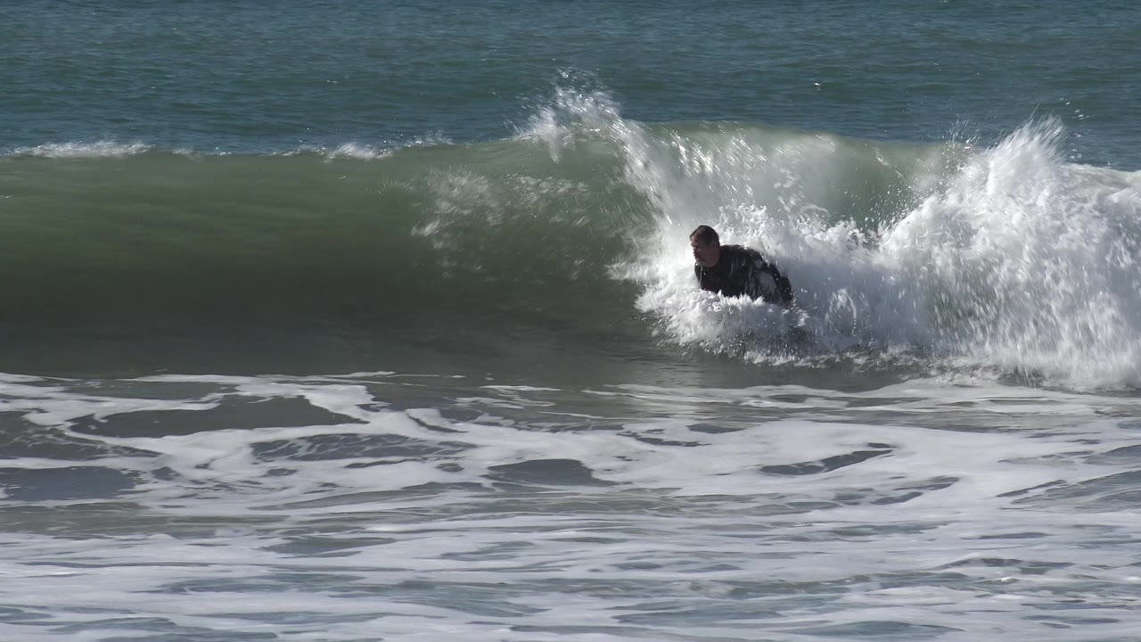 At Huntington Beach, California, the surfer appears near the right side of the frame beside a collapsing section of wave and bright white spray.