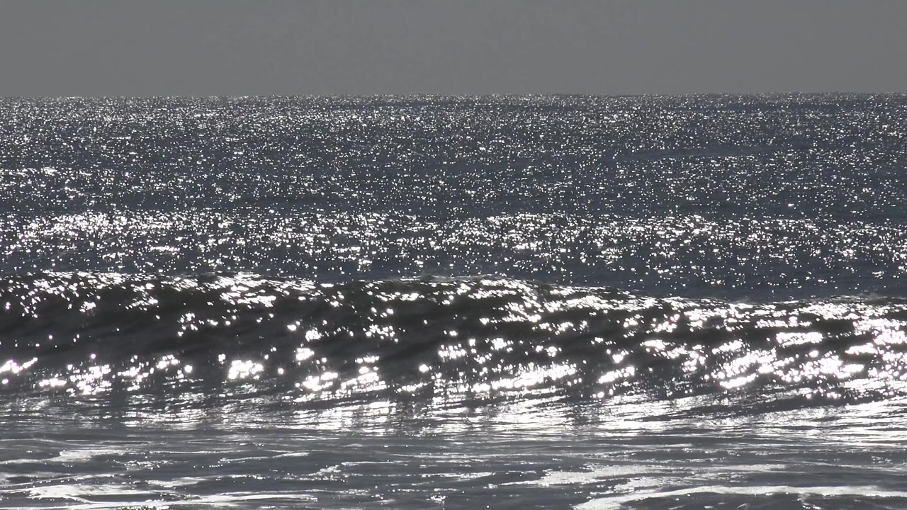 Huntington Beach ocean surface glittering in strong sunlight, with a dark wave line forming across the midground and no visible people.