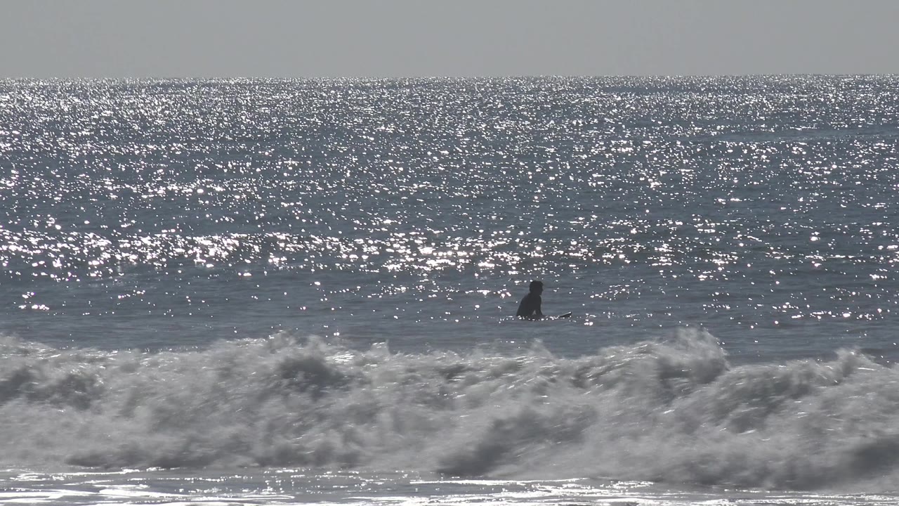 Small surfer silhouette in open water behind shore break.