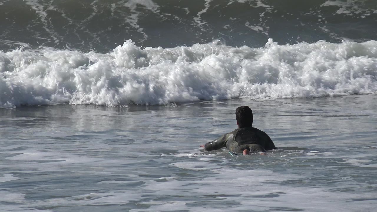 The surfer remains mid-frame on the board while a foamy wave line stretches across the upper frame at Huntington Beach, California.