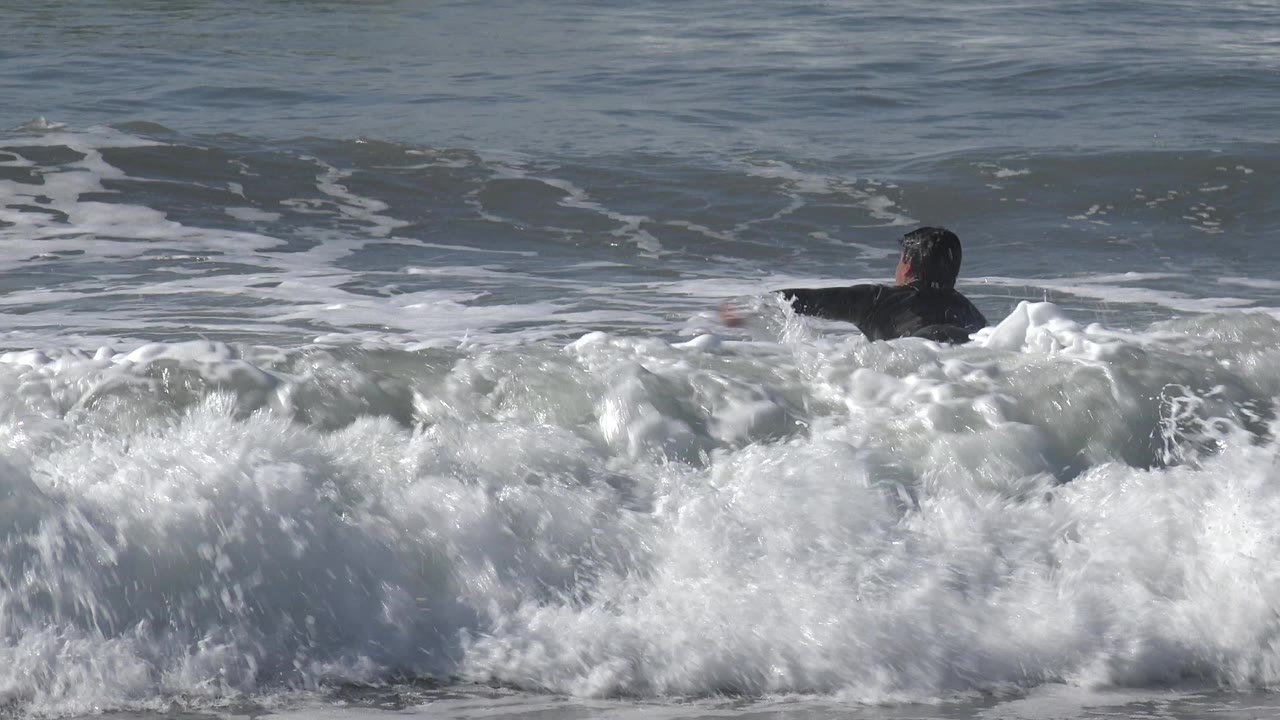 The surfer remains in the midground at Huntington Beach, with white surf rising across the foreground and open water behind.