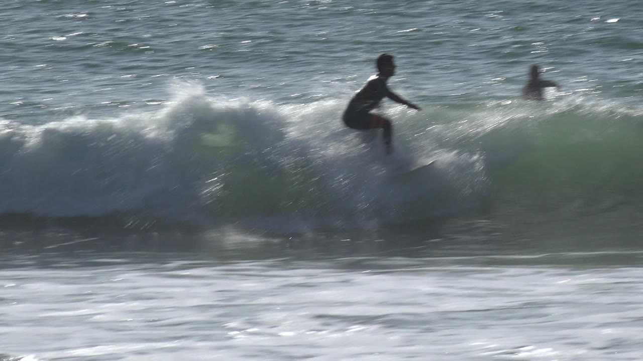 Surfer riding a small wave with another person in the water behind.