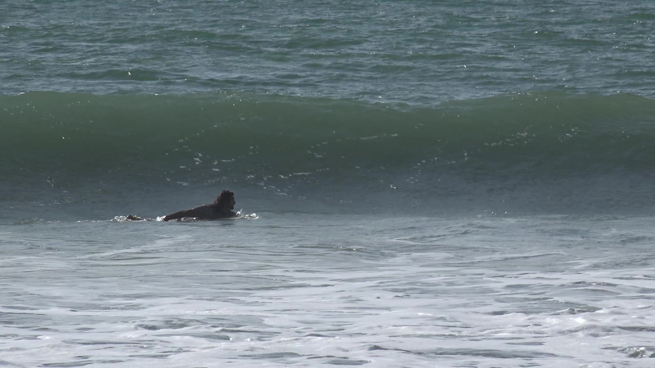At Huntington Beach, California, the surfer is still distant and low against the water while the wave face darkens and begins to pitch forward.