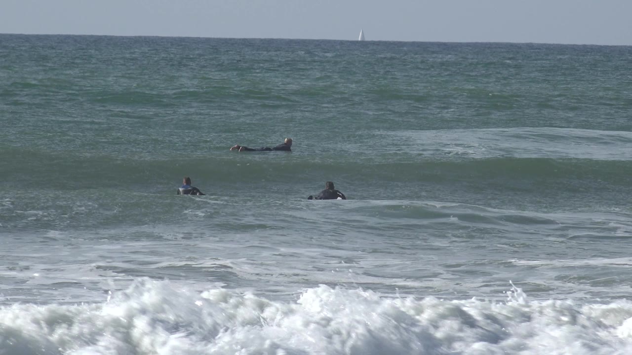 Several surfers on boards beyond a breaking wave.
