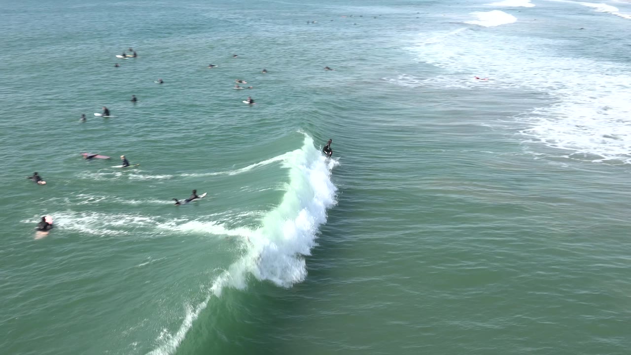 At Huntington Beach, the wave curls farther across the frame as a surfer stays near the crest and several distant surfers remain positioned in the surrounding water.
