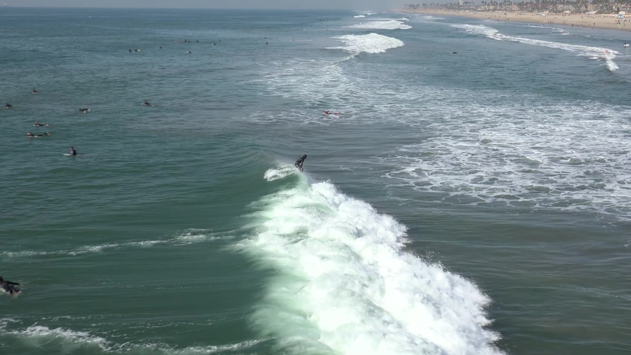 Surfer rides near the top of a foamy wave with shoreline in the distance.