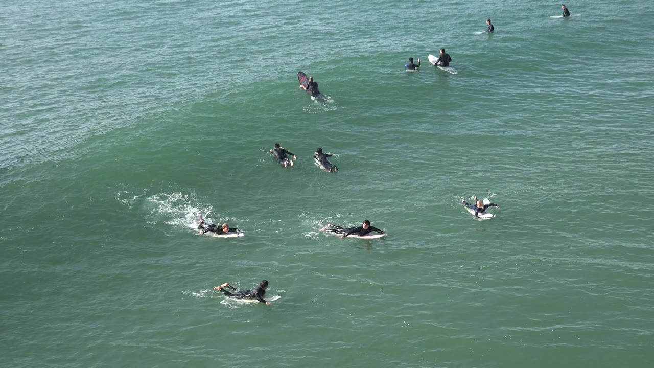 Surfers cluster near whitewater and open water.