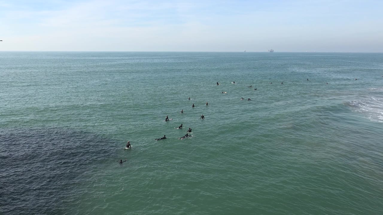 Surfers cluster in open water beneath a pale horizon.