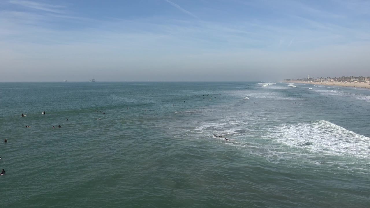Wide ocean view with breaking surf and distant swimmers near the shoreline.