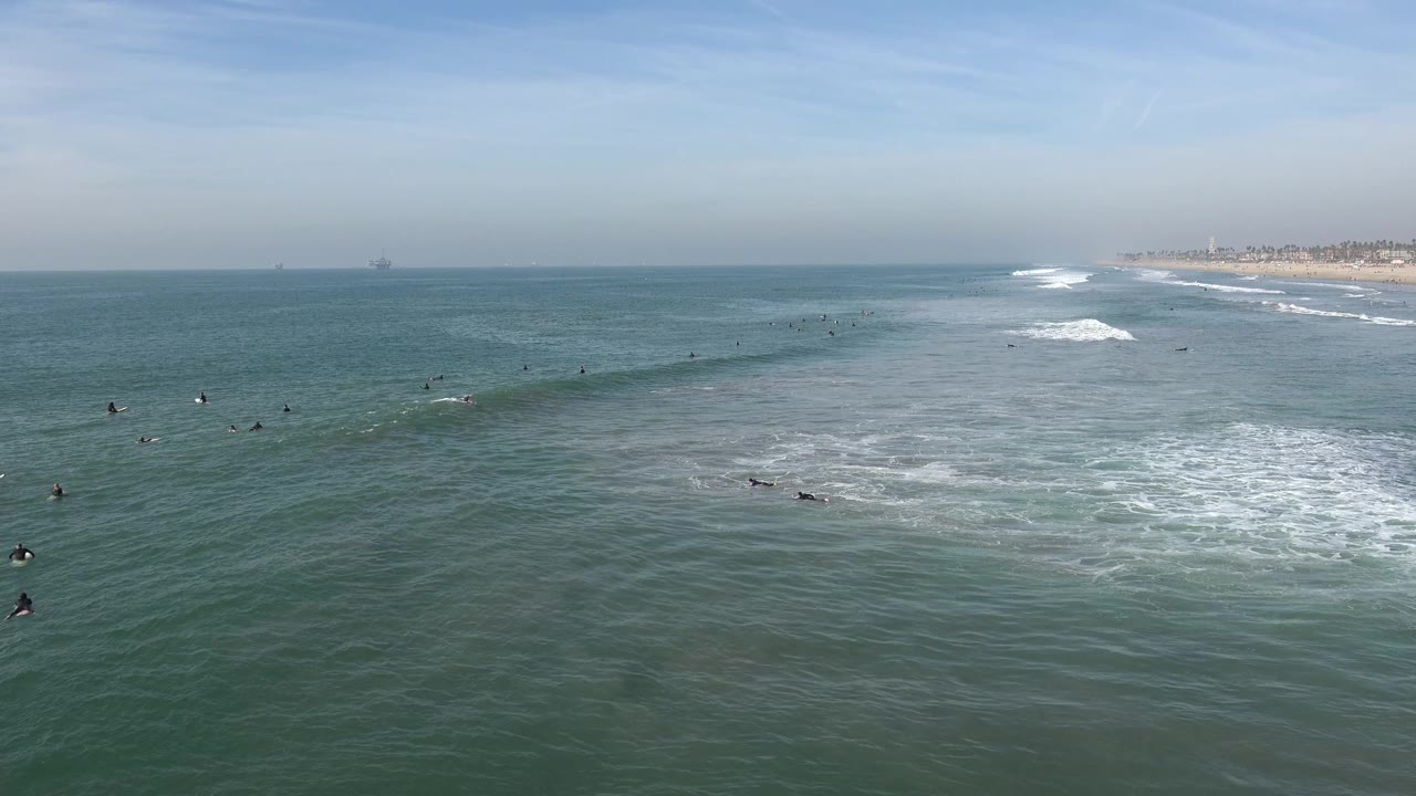 Distant surfers sit in green-blue water as waves break toward shore.