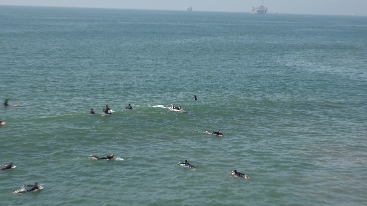 Surfers paddle and wait offshore with small patches of white water.