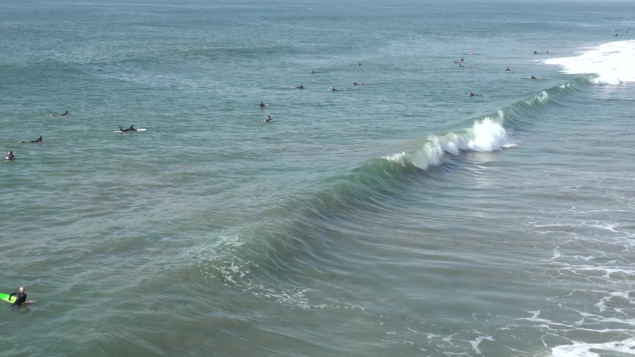 Whitewater spills from a breaking wave with surfers beyond it.