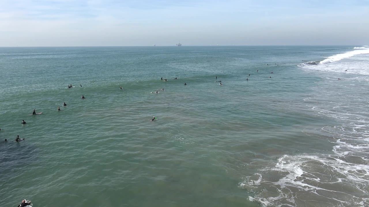 Ocean surface with surfers and foam patches under a pale sky
