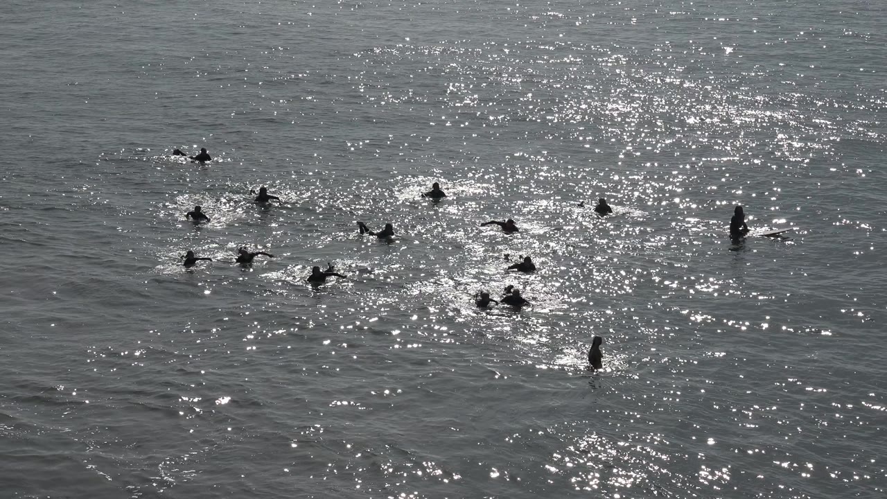 At Huntington Beach, California, distant people are dispersed across the frame, with sparkling reflected light strongest on the right half of the water.