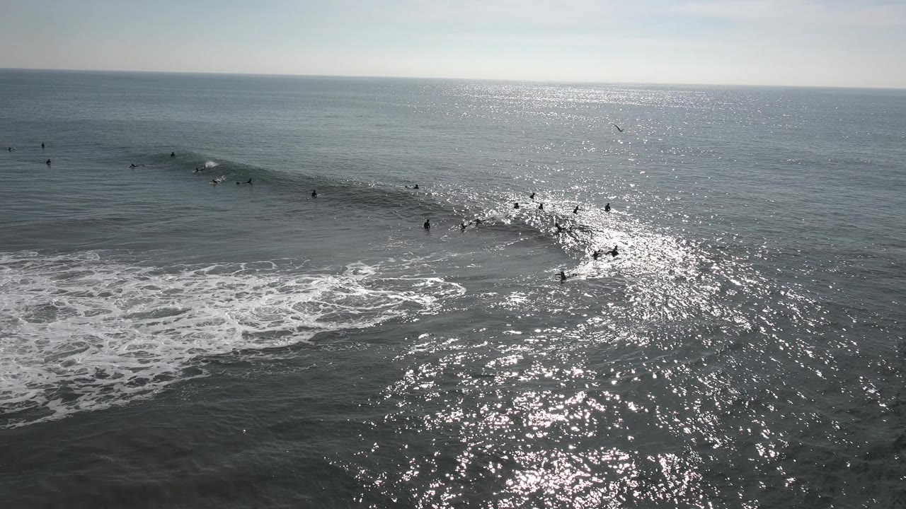 A wave rolls toward shore as surfers sit and paddle around the break.
