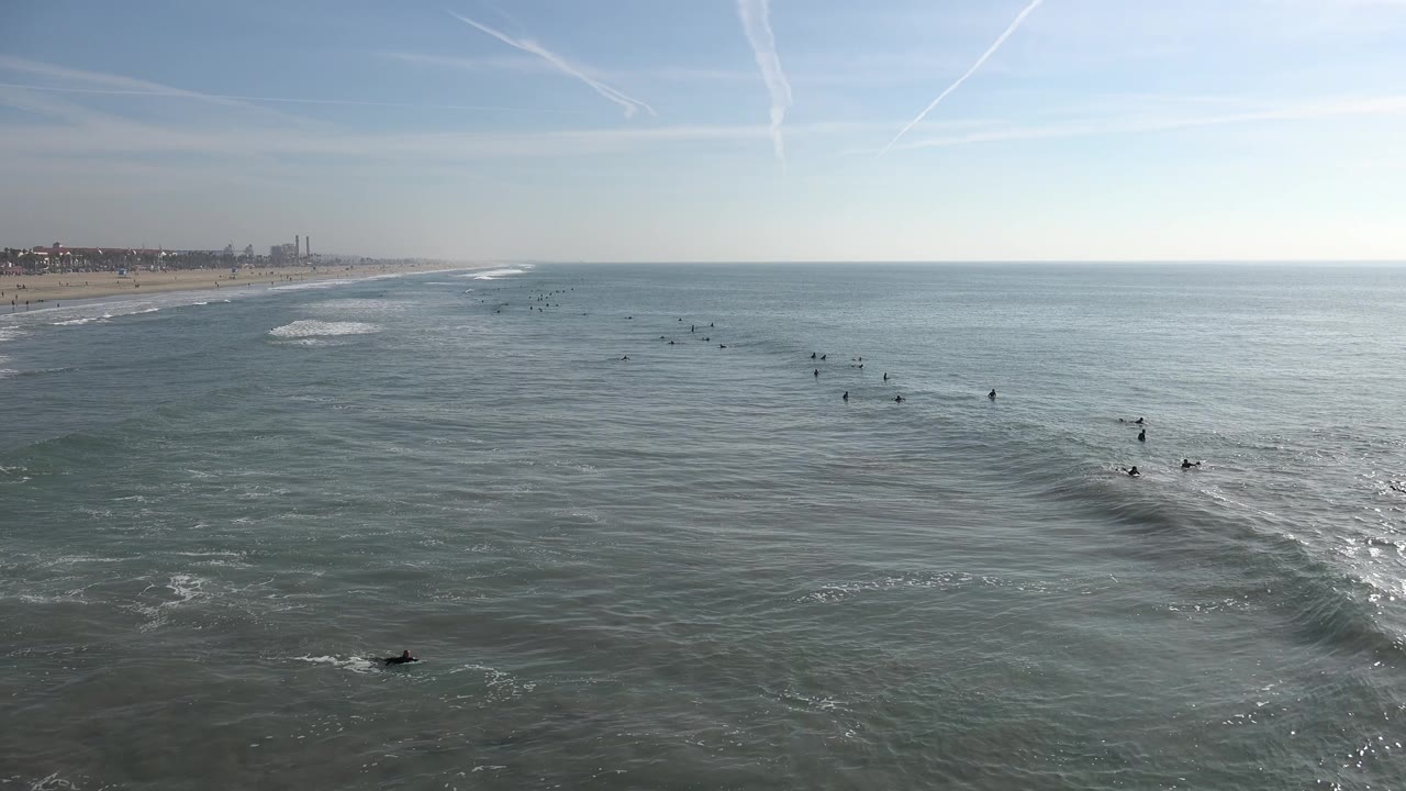 Wide shoreline and ocean view with surfers near rolling waves.