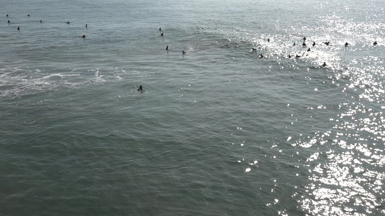 Surfers spread across open water with bright glare below them.