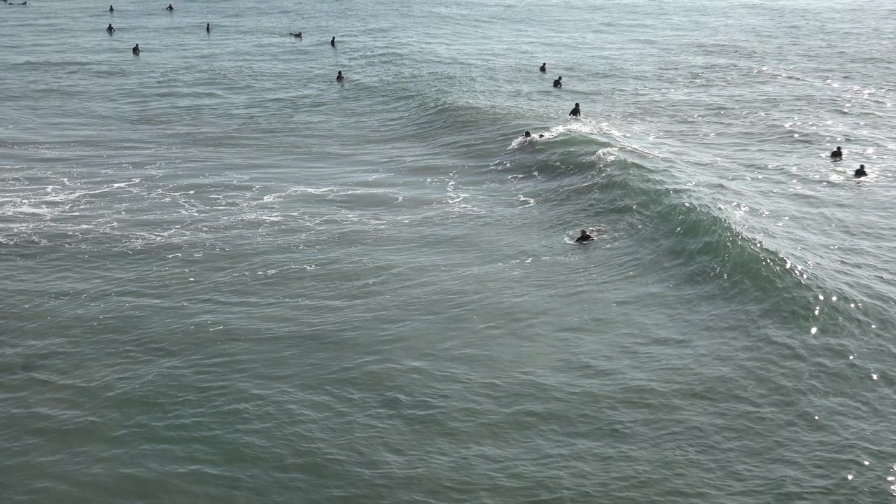 Ocean wave cresting with surfers nearby.