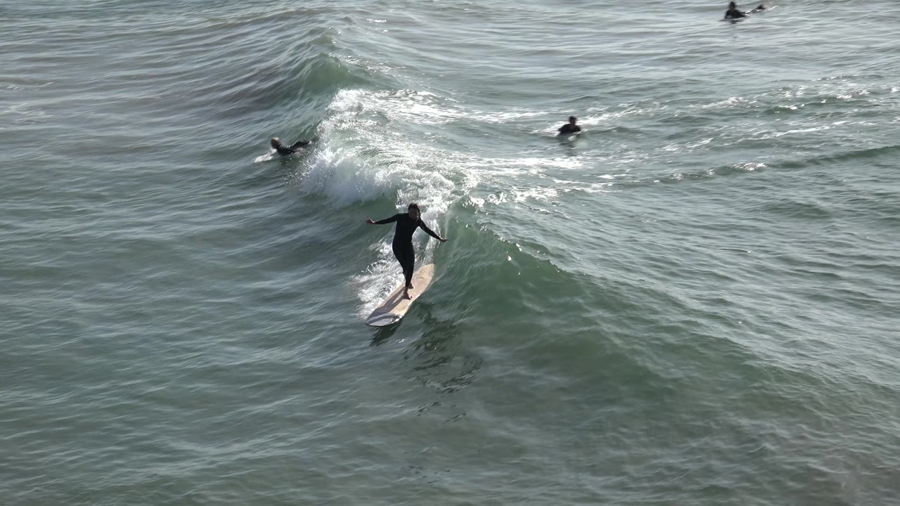 Surfer gliding down the wave with distant surfers in the water.