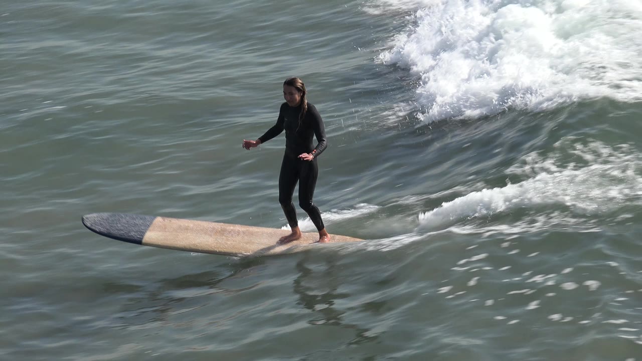 Surfer balancing on a longboard as foam trails behind.