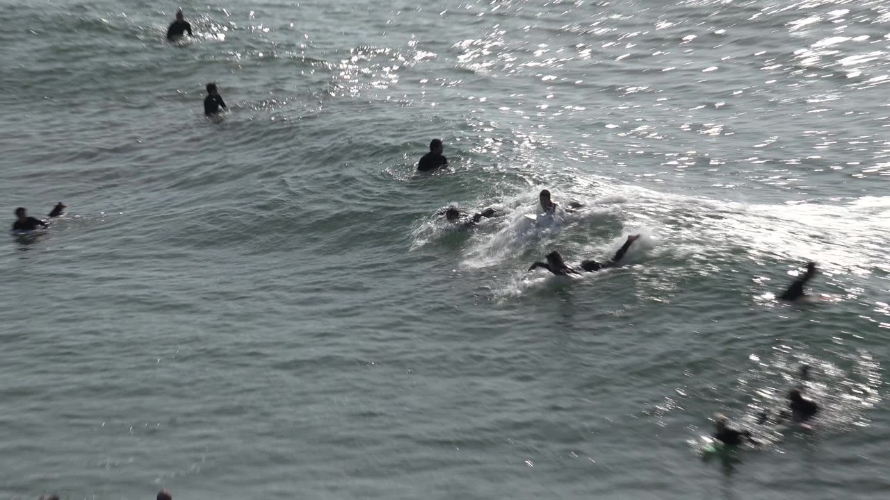 A tighter view shows several surfers near a breaking wave at Huntington Beach, with foam forming around paddlers and boards.