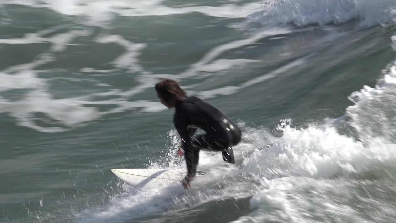 Surfer crouched near the front of a white board in foamy water.