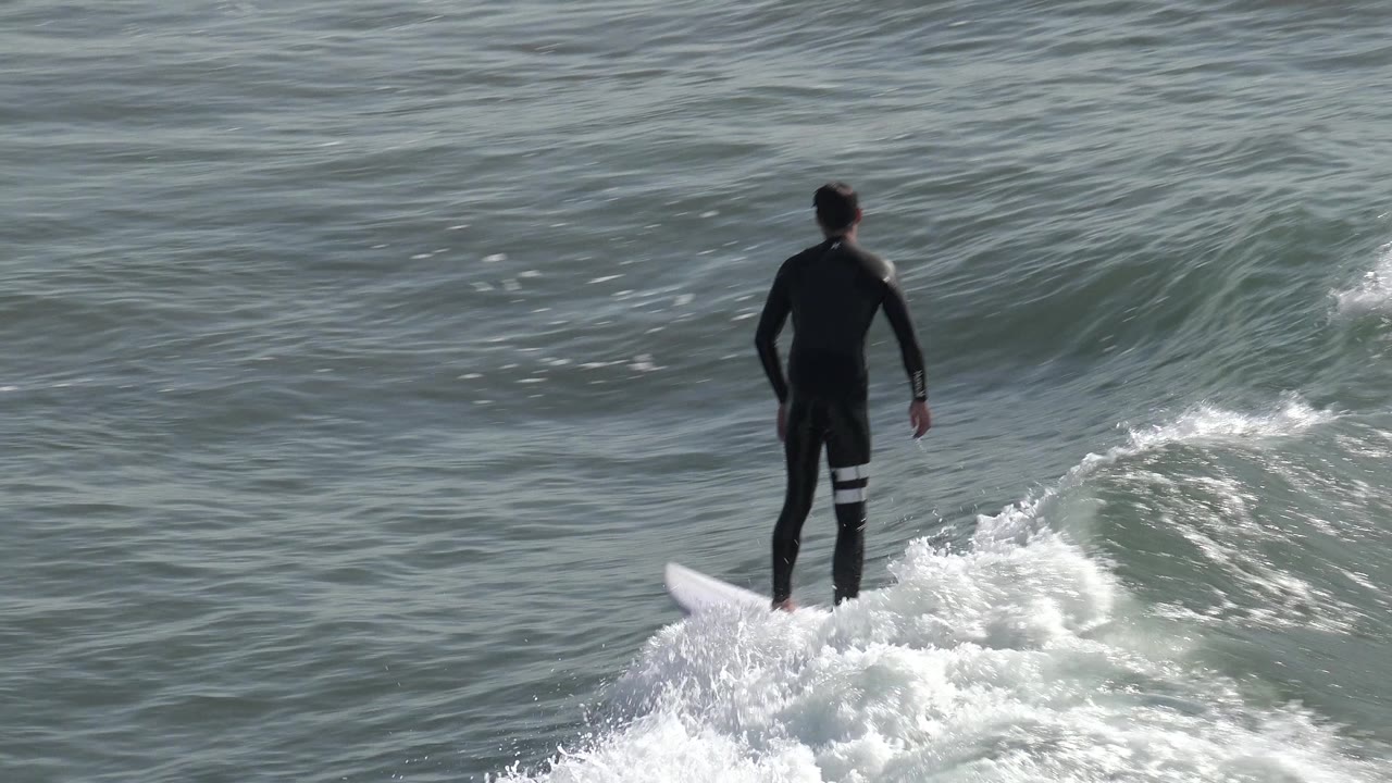The Huntington Beach surfer remains upright on the board while a small curling wave forms ahead and white foam trails behind.